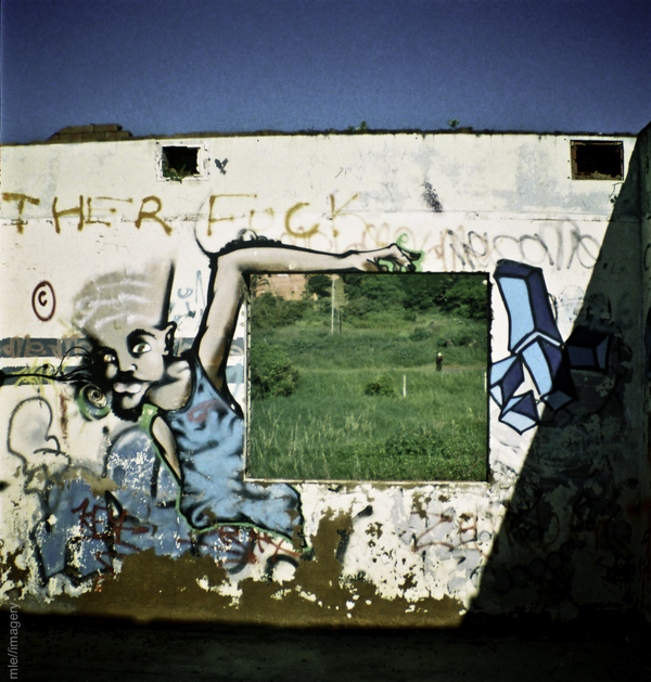 Lady waiting in the road for a taxi to Durban as seen through a broken window in a broken house